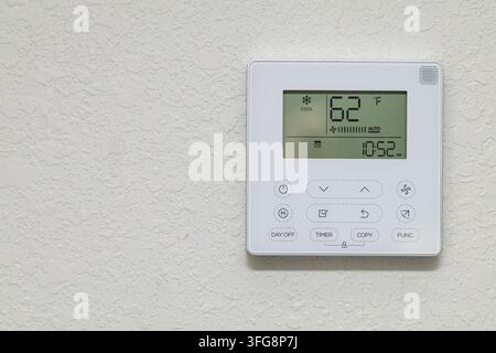 Wall-mounted air conditioning controller displaying 62°F in cool mode, featuring timer and fan settings on textured interior wall. Stock Photo