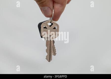 Two metal keys held by hand on key ring, isolated against light neutral background Stock Photo