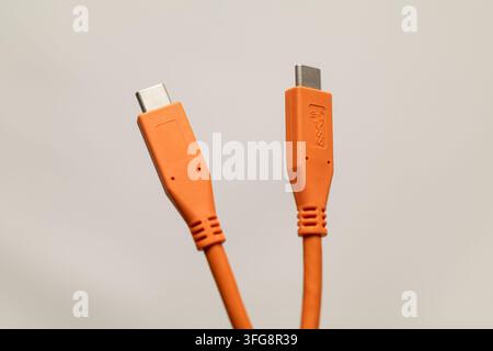 Orange USB-C to USB-A cable connectors isolated against neutral background, showing different plug designs and detailed molded housings. Stock Photo