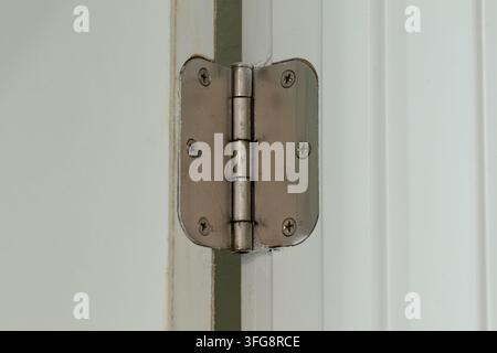 Close-up of metal door hinge secured with screws on white painted door frame, showing hinge mechanism and hardware detail. Stock Photo