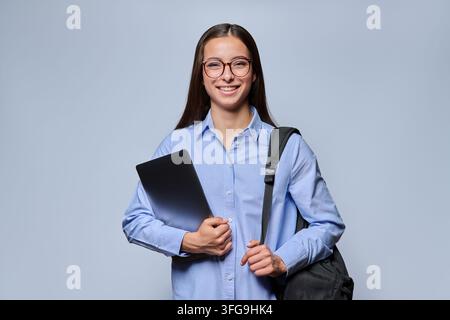 Smiling young woman student in glasses holding laptop and backpack studio shot Stock Photo