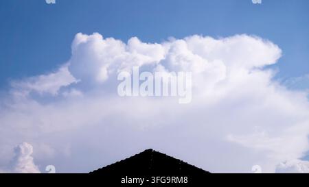 Large White Cumulus Cloud Above Residential Rooftop And Blue Sky Stock Photo