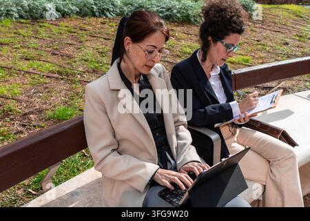 Businesswomen collaborating outdoors using tablet and clipboard Stock Photo