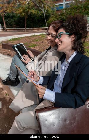 Businesswomen collaborating outdoors using tablet and clipboard Stock Photo
