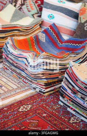Colorful stacks of woven rugs at a market in a sunny location Stock Photo