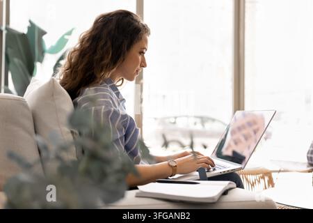 Focused female freelancer typing on laptop at home office Stock Photo