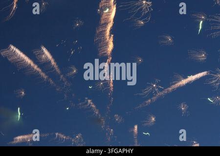 A vibrant fireworks display with multiple explosions creating dynamic lines and bright trails across the evening sky. Stock Photo
