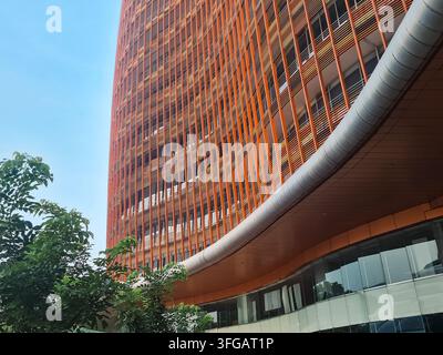 Low-angle shot of a modern orange skyscraper with vertical slats and curved architecture under a clear blue sky. Stock Photo
