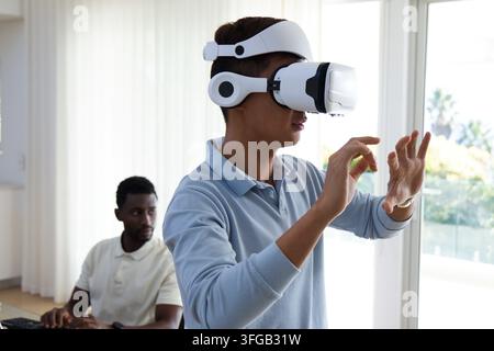 Diverse male coworkers testing VR interface in bright home office with white headset, keyboard Stock Photo