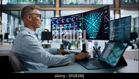 Data Scientist In Lab Coat Analyzing Neural Network Models On Dual Laptops. Stock Photo