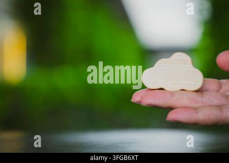Cloud computing and sustainable IT concept with hand holding wooden symbol against lush green nature bokeh background for digital storage, eco data Stock Photo