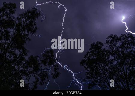 Dramatic lightning storm with powerful flashes illuminating the city skyline and dark stormy night clouds above. Stock Photo