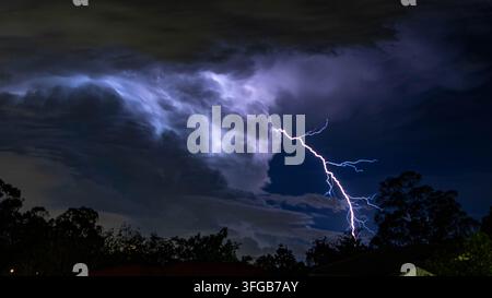 Dramatic lightning storm with powerful flashes illuminating the city skyline and dark stormy night clouds above. Stock Photo