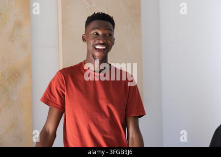 Adult man standing and smiling while wearing red T-shirt in studio room with vertical wall panels Stock Photo
