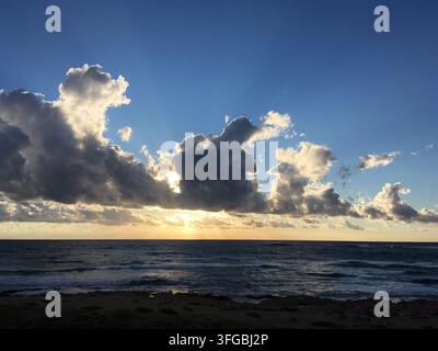Sunset in Paphos, Cyprus, March 2019. The sky features large, dramatic clouds with the sun partially hidden, casting rays of light. The horizon is mar Stock Photo