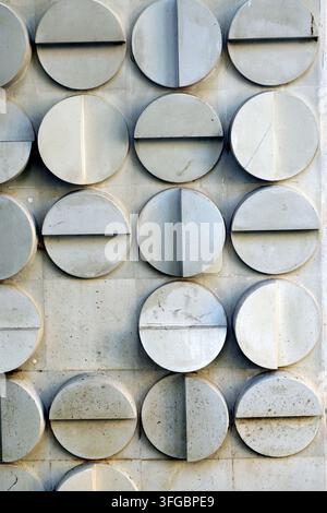 Grey concrete wall with repetitive 3d circular reliefs, some split horizontally or vertically, creating a modern, minimalist architectural texture wit Stock Photo