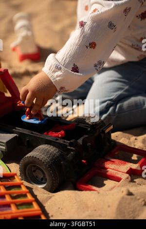 a warm, abstract closeup collage captures a hand holding a tiny colorful toy over blurred floral fabric, with red and blue details, dark workshop tool Stock Photo