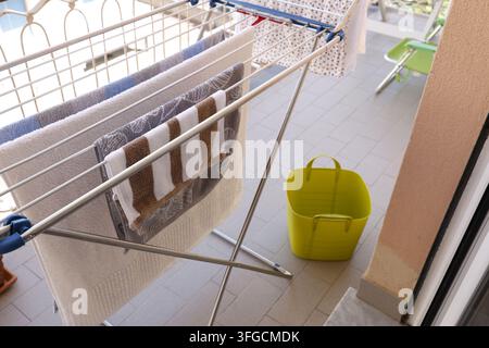 Wet laundry drying on metal clothes rack standing on balcony floor.  Stock Photo