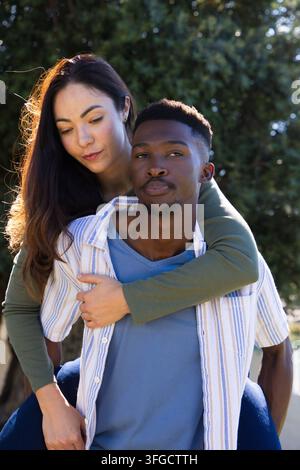 Couple with African American man carrying Asian woman, wearing striped shirt and blue tee in park Stock Photo