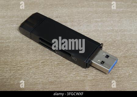 Angled perspective close-up of a black USB multi-card reader showing memory card slots and USB connector on a wooden surface. Stock Photo