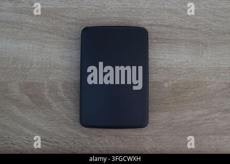 Rectangular black electronic storage device centered on a neutral wood texture background, commercial flat lay shot. Stock Photo