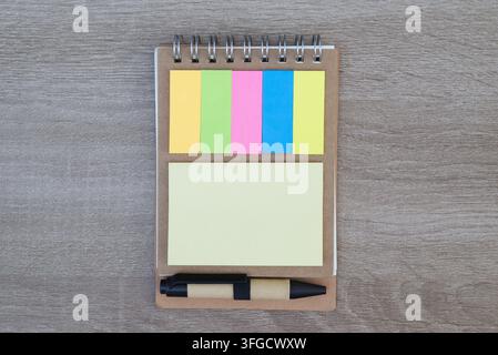 Top-down view of a spiral notebook with colorful sticky notes, a yellow memo pad, and a pen on a light wooden background. Stock Photo
