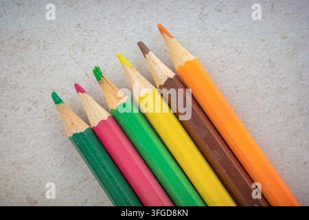 Six colored pencils in a row show various colors like green, yellow, and orange on a light surface. This captures a simple moment of art supplies read Stock Photo