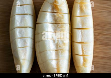 Three freshly cut slices of juicy yellow melon placed on a round wooden chopping board. The melon pulp is sliced into convenient bite-sized pieces. Stock Photo