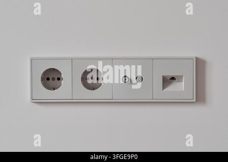 White wall outlet panel on clean interior wall with flush faceplate. Includes two round power sockets plus coax connector and ethernet data jack in sl Stock Photo