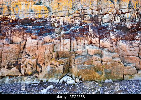 Coastal Rocky Cliff With Colorful Lichen and Weathered Stone Texture on Pebble Beach. Stock Photo