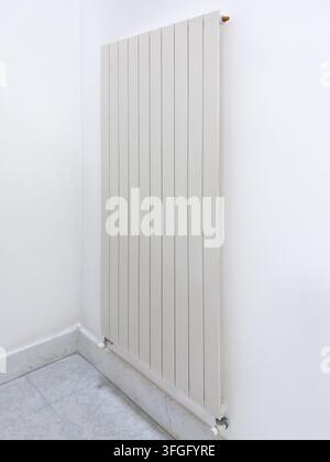 Side view of a sleek, white vertical flat-panel radiator installed on a clean white wall in a modern room with marble flooring. Perfect concept for co Stock Photo