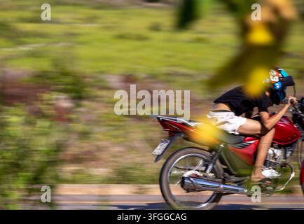 High-speed action capture of a young man riding a red motorcycle with motion blur background framed through green foliage Stock Photo