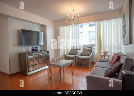 Cozy Living Room Ambiance: A stylish living room featuring a comfortable sofa, elegant armchairs, a mirrored dresser, and a chandelier Stock Photo