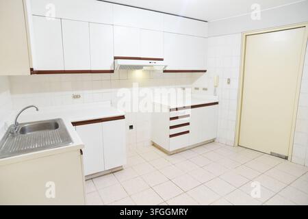 Clean Kitchen Interior: A bright and spacious kitchen featuring clean white cabinetry, tiled flooring, and a functional sink area Stock Photo