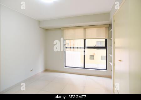 Empty Room with Window: An empty, minimalist room features a large window offering a view of an urban landscape, complemented by a closet and built-in Stock Photo