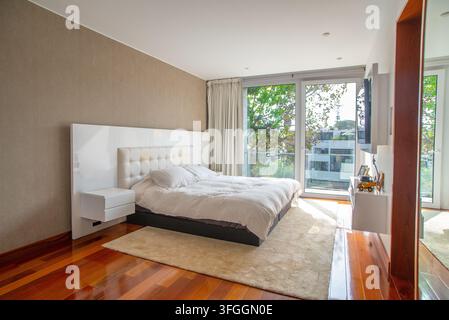Modern Master Bedroom with Balcony View: A luxurious and contemporary master bedroom featuring a plush white bed, sleek nightstands. Stock Photo