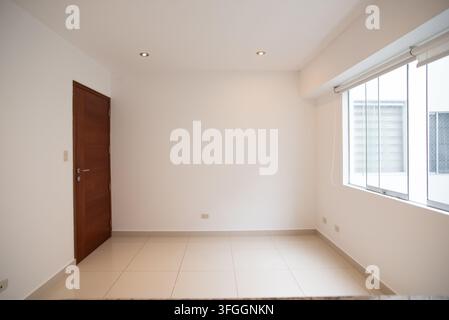 Empty Room with Window and Door: A bright, empty room features a wooden door and a large window, offering a clean slate for design and renovation Stock Photo