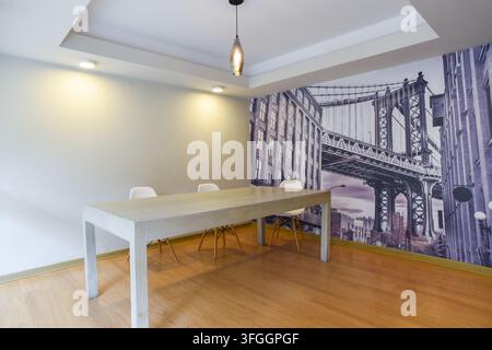 Modern Dining Room with Cityscape Mural: A minimalist dining room features a sleek white table and chairs, accented by a dramatic mural of a city sky Stock Photo