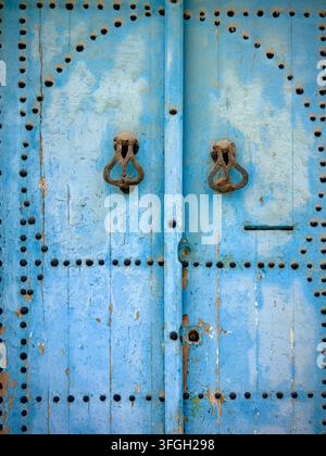 Weathered blue wooden door with metal studs and traditional knockers in the historic Medina of Sousse, Tunisia. Stock Photo