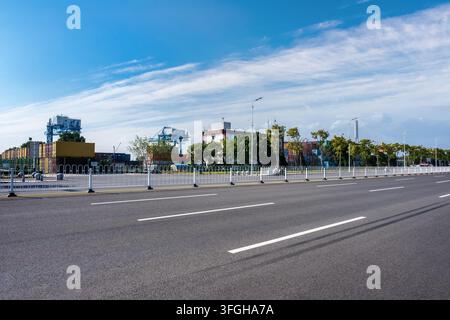 container terminal at Anqing Port, featuring large cranes and containers in the background. the foreground shows an empty asphalt road with clear lane markings, the overall scene highlights the infrastructure of a modern port facility, China Stock Photo
