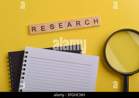 Research concept with magnifying glass, notebook, and research text on yellow background, representing investigation, analysis, data collection, study Stock Photo