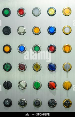A display panel featuring a grid of various colorful industrial push buttons, indicator lights, and rotary selector switches for machinery control and Stock Photo