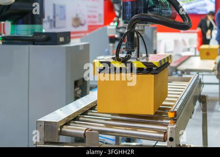 Automated robotic arm using vacuum suction cups to lift and move a brown cardboard box along a roller conveyor belt in a modern logistics or manufactu Stock Photo