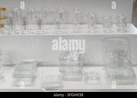 A display shelf showing an assortment of empty clear plastic food packaging containers, including cups with dome lids and various boxes for catering. Stock Photo