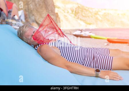 Man beach relaxation as middle aged man in striped swimsuit relaxes on a blue beanbag with a red net on a sunny beach Stock Photo