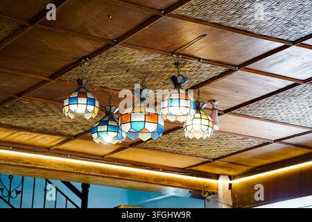 Hanging stained-glass lamps with geometric patterns on a wooden ceiling, creating a warm and artistic interior atmosphere. Stock Photo