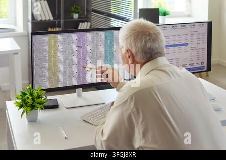 Senior accountant analyzing spreadsheets on dual monitors in bright modern office Stock Photo