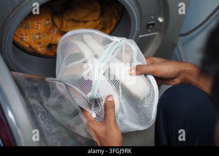 Putting Sneakers in Mesh Laundry Bag Before Washing in Front-Load Washing Machine at Home Stock Photo