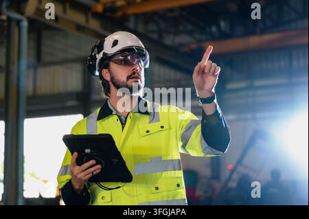 Industrial engineer in safety jackets pointing inside factory plant while using digital tablet. Concept of logistics workflow planning, supply chain c Stock Photo