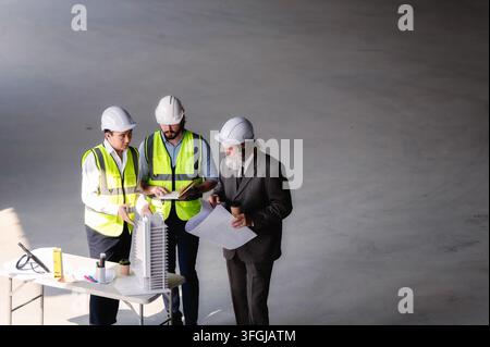 Real estate developers examining architectural model at empty space floor in building construction site, High angle view senior site managers and engi Stock Photo